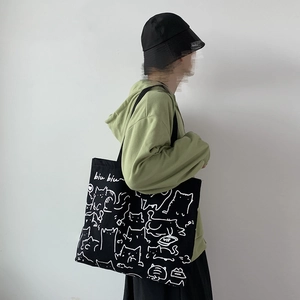 Detail of a black canvas tote bag featuring a cute cat illustration and biu biu text
