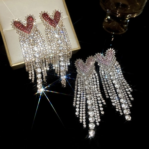 Detailed view of red and pink heart tassel earrings with sparkling rhinestones on black
