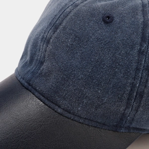 Detail of wool fabric and black leather brim on a contrast stitch baseball cap