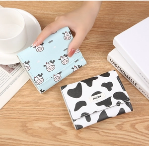 Detail of short tri-fold wallets featuring cute cow prints and milk labels on wood surface