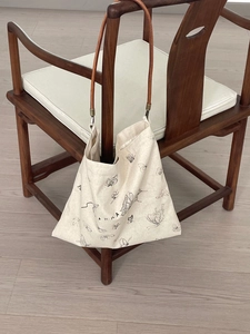 Close-up of butterfly print canvas tote with slim brown leather handles on wooden chair