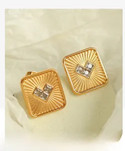 Detail of square gold earrings with sunburst texture and heart-shaped crystals