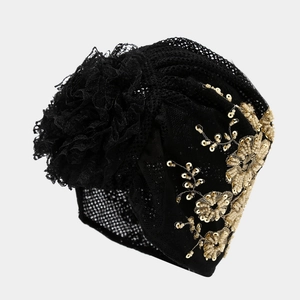 Black lace turban with 3D floral design and gold sequin beadwork on grey background