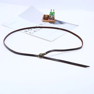 Detail view of narrow dark brown leather belt featuring a round brass buckle and rivet