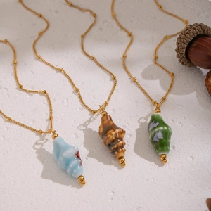 Three gold beaded necklaces with colorful conch shell pendants in blue, brown, and green