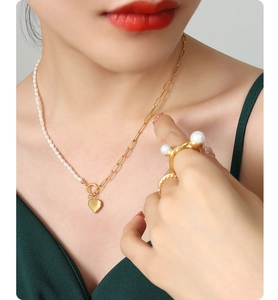 Detail of elegant gold necklace featuring freshwater pearls and a heart pendant on a model
