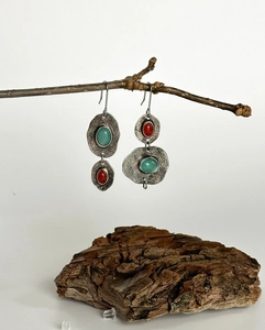 Vista macro de pendientes boho asimétricos con turquesa y coral sobre fondo de madera