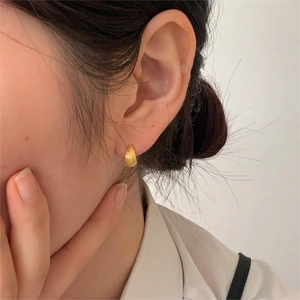 Close-up of minimalist gold shell earrings with fine radial textures worn on a female ear