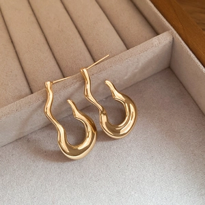 Macro shot of gold liquid-style irregular hoop earrings resting on beige velvet padding