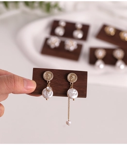Close-up of vintage gold coin earrings with pearls and long chain on wood display