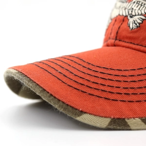 Close-up of orange baseball cap featuring eagle embroidery and black brim stitching