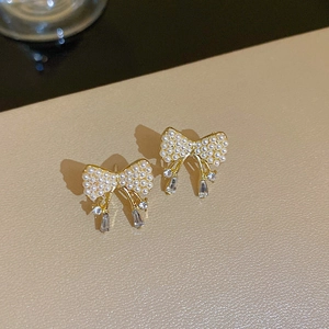 Detailed macro view of gold bow earrings with pearl inlay and dangling zircon stones