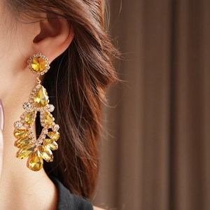 Close-up of gold tassel earrings with yellow crystals worn by a model in soft light
