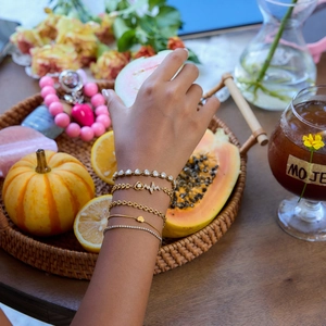 Lifestyle shot of layered gold heart and tennis bracelets worn in a resort setting