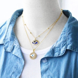 Detail view of 18K gold plated double layer necklace with blue enamel evil eye pendants