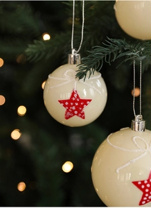 Close-up of cream Christmas ball with red stars and glitter details on a festive tree