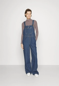 Detail of blue denim overalls with front pocket and adjustable metal buckles on strap