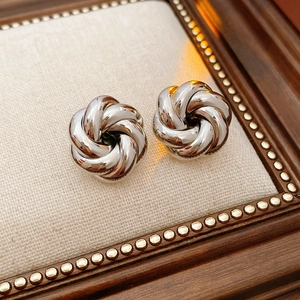 Detailed view of silver knot swirl stud earrings on textured fabric and vintage frame