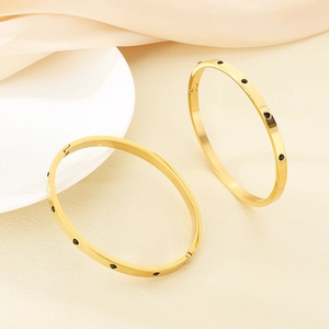 Detail of gold bangles with black crystal inlay on beige silk and ceramic decor