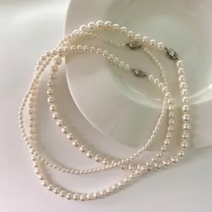 Detailed view of three white pearl necklaces with metallic clasps in a ceramic tray