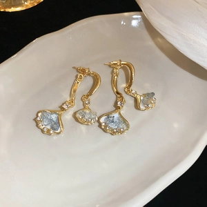 Macro detail of golden ginkgo leaf earrings with blue crystals on a ceramic tray