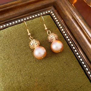 Close-up of elegant gold hollow bead earrings with large pink pearl pendants on green velvet