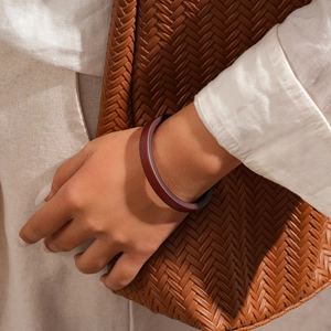 Detail of dark red resin bangle worn on wrist paired with brown woven bag and linen