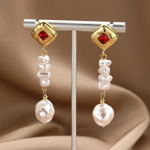 Detail of gold drop earrings featuring red square gems and baroque pearls on silk