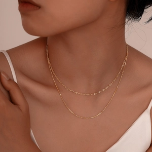 Detail of layered gold paperclip and snake chain necklace on model neck