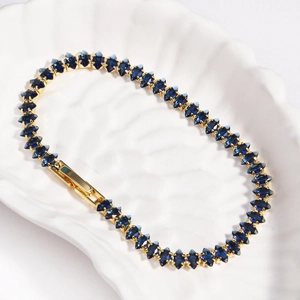 Detail of gold tennis bracelet with dark blue marquise cut stones on a white tray