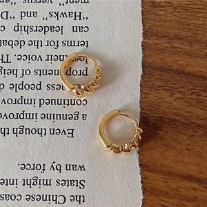 Close-up of golden twist hoop earrings on vintage paper and wood background