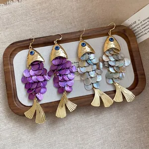 Elegant fish-shaped shell tassel earrings in purple and white on a wooden tray