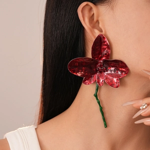 Detailed view of oversized red orchid flower earrings with a wavy green stem drop