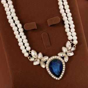 Gros plan du collier de perles à double rangée avec pendentif larme bleue sur support velours