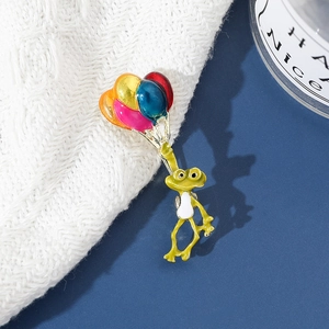 Détail d'une mignonne broche émaillée grenouille et ballons sur un pull en maille blanc