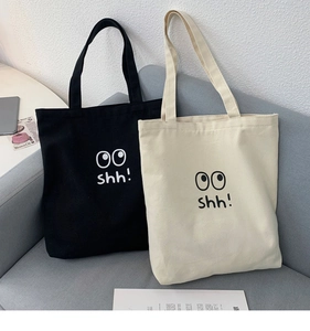 Primer plano de bolsos tote de lona negros y beige con estampado de ojos en un sofá