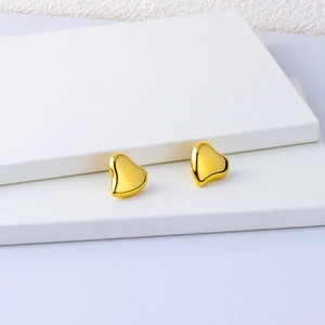 Polished 18K gold irregular heart stud earrings in stainless steel on white pedestal
