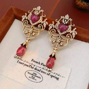 Detail of vintage gold earrings with red heart crystals and water drop gems in a jewelry box
