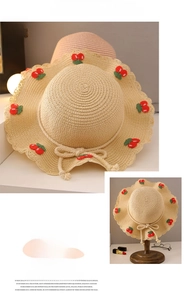 Detail of children's straw hat featuring cherry embroidery and wavy edges for summer sun