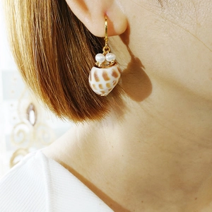 Detail shot of golden shell earrings featuring white pearls and natural tiger-striped shells