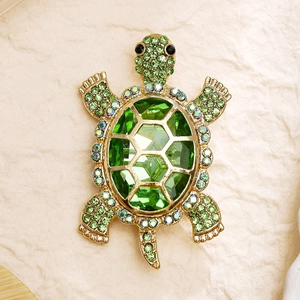 Detailed close-up of a vintage golden turtle brooch with vibrant green crystals and rhinestones
