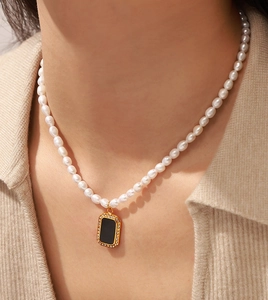 Detailed view of pearl necklace with gold-rimmed black pendant on model neck