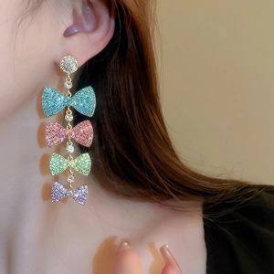 Detail of colorful bow fringe earrings with rhinestones showing full dangling length on ear