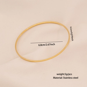 Top view of a thin golden stainless steel bangle with a diameter of 6.8cm on a textured surface