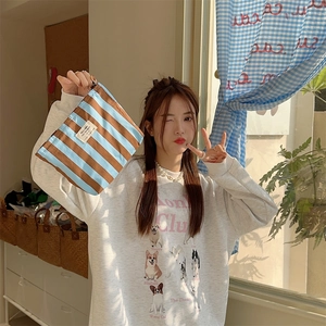 Blue and brown striped canvas cosmetic bag held by a model in a cozy indoor setting