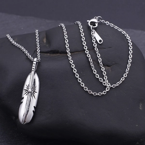 Minimalist stainless steel feather pendant necklace displayed on a dark natural stone