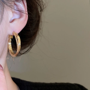 Macro shot of triple layered gold crossover hoop earrings worn on a model's ear