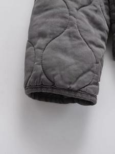 Macro detail of dark grey quilted jacket cuff with double-stitched twill texture