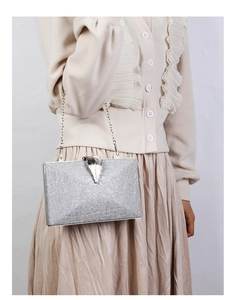 Silver glitter clutch bag with leaf clasp and chain strap worn with elegant outfit