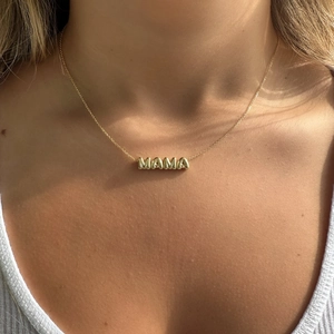 Primo piano di una persona che indossa una collana con ciondolo MAMA dorato sulla pelle